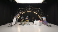 Indoor setup of Konligo event structure featuring two cyclists on stationary bikes and a display table with helmets and water bottles. Now available on MTN Shop US.
 - imagen 4